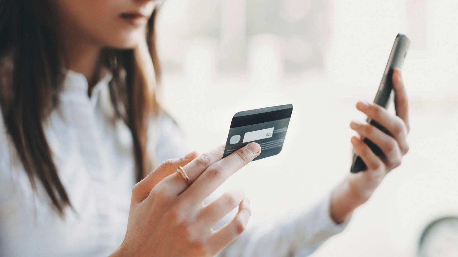 Vista lateral das mãos de uma mulher segurando um cartão de crédito de plástico enquanto na outra mão um smartphone interno